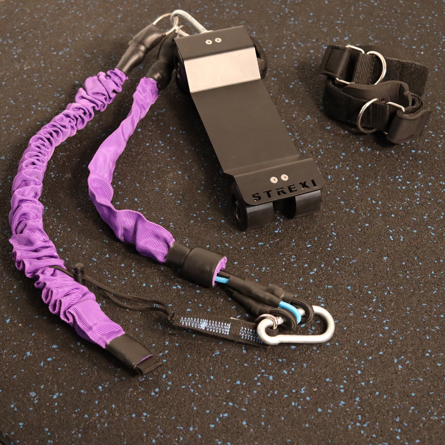 A split machine named Strexi, along with its purple adjustable safety harness, bands, ankle straps, and a clip shut mechanism.